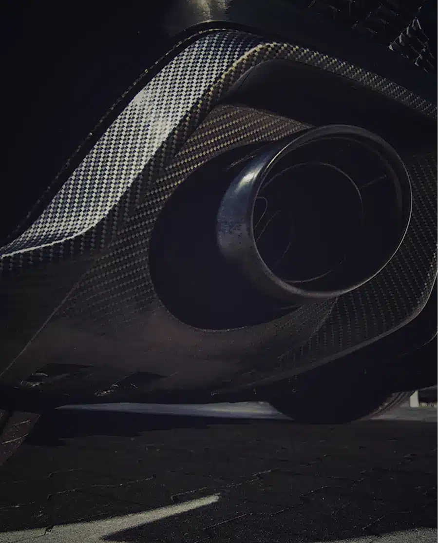 Nahaufnahme des hinteren Stoßfängers und des Auspuffrohrs eines Autos aus Kohlefaser, wobei Licht und Schatten die Textur und die Designdetails hervorheben.