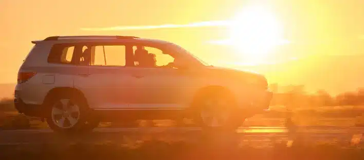 A silver SUV drives along a road at sunset, with the sun low in the sky, casting a warm golden light—perfect for an unfallgutachter Dresden or kfz sachverständiger to capture details for a precise schadensgutachten.