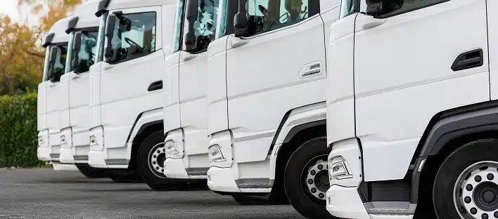 A row of white semi-trucks is parked closely side by side, showing the front and side view of each vehicle—perfect for a kfz sachverständiger conducting a detailed schadensgutachten on the truck cabs and front wheels.