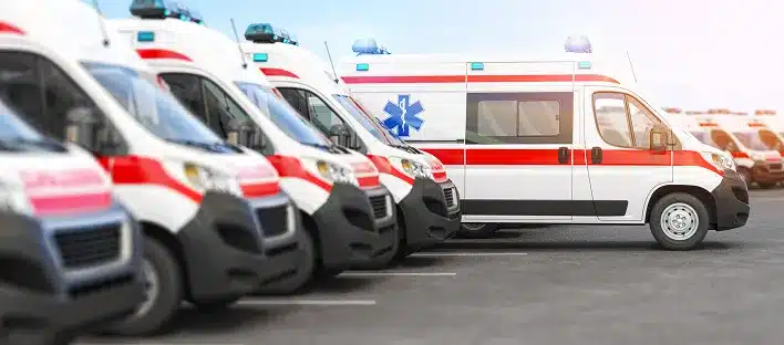 Several ambulances with red and white stripes are parked in a row in a parking lot under daylight, watched over by an unfallgutachter Dresden ensuring every schadensgutachten is thorough and precise.